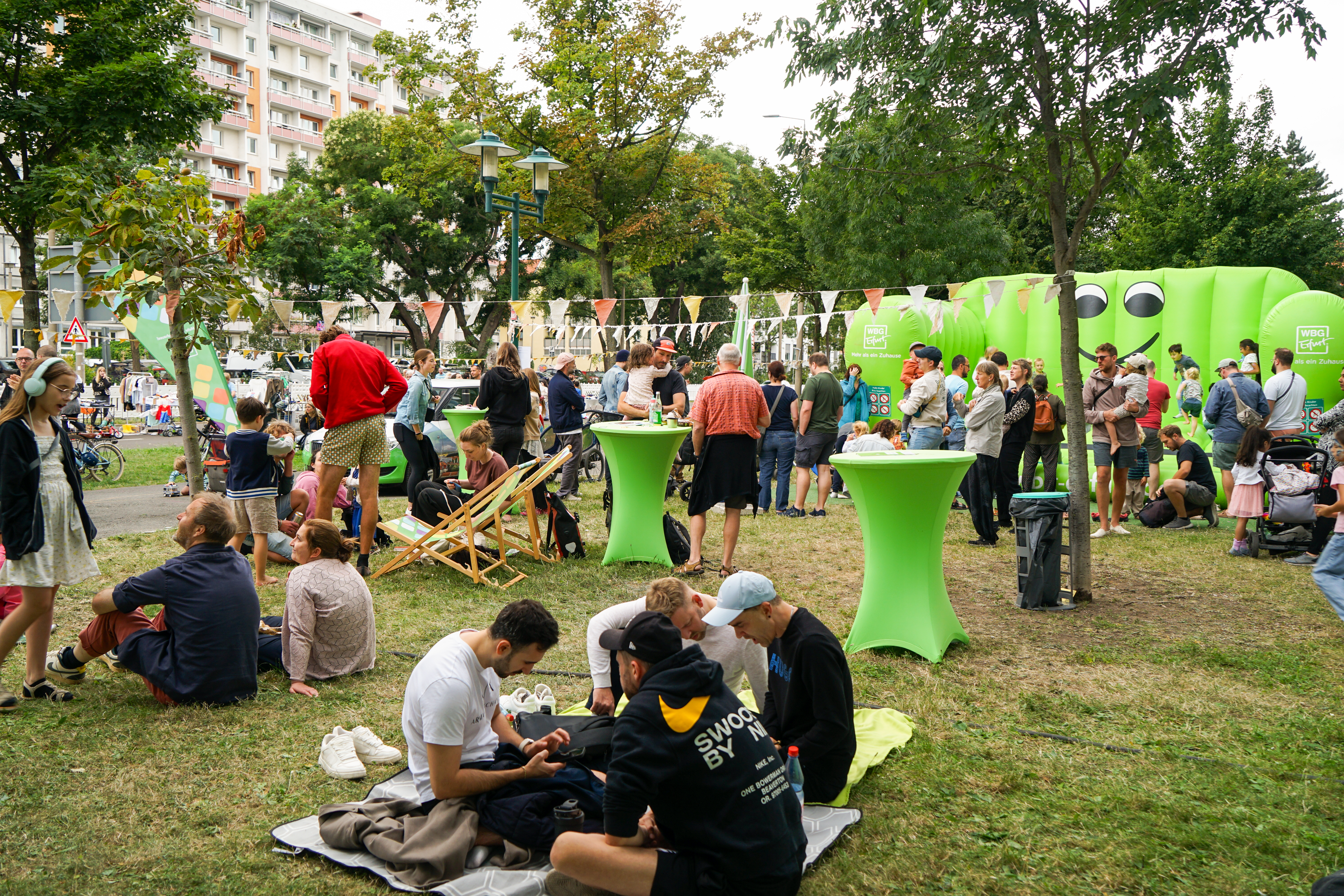 Besucher beim Hebebühnenkonzert Menschen sitzen und stehen auf einer Wiese zwischen grünen Stehtischen