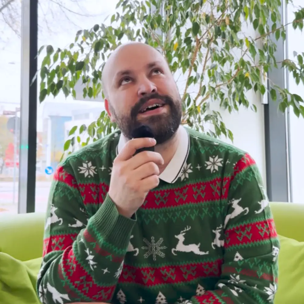 Mann in weihnachtlichem Pullover hält ein Mikrofon und lächelt