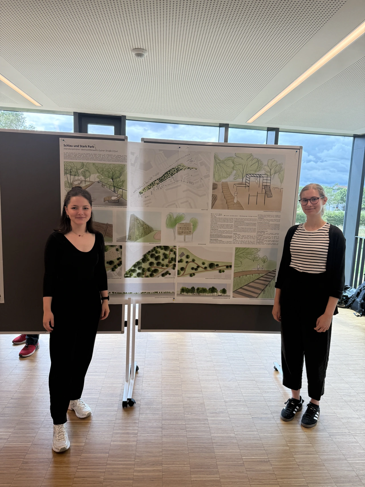Architekturpräsentation Györer Straße Zwei junge Frauen präsentieren ein Architekturkonzept mit Plakaten auf einer Stellwand in einem hellen Raum