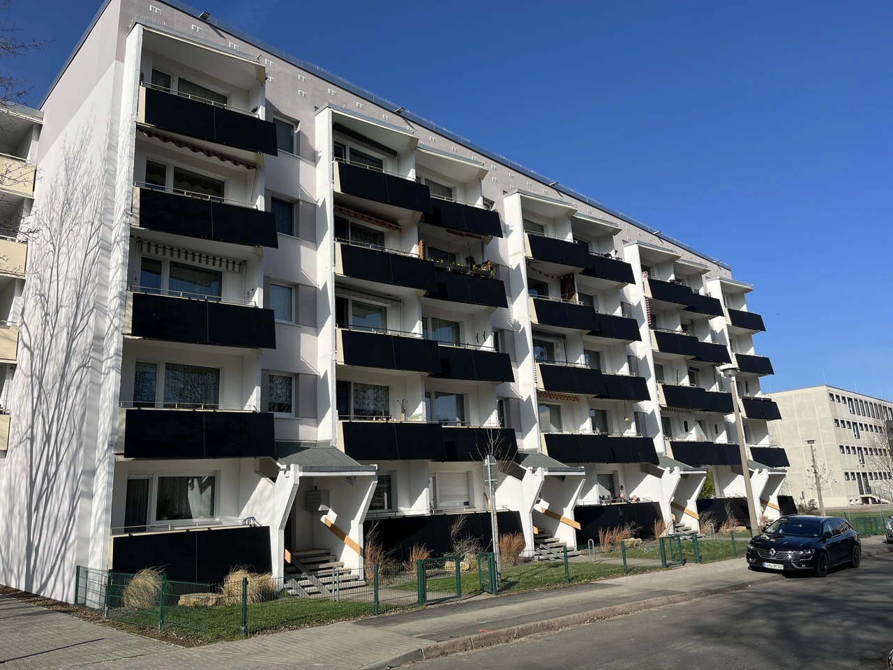 Balkonkraftwerke Mehrfamilienhaus Weißes Mehrfamilienhaus mit Balkonkraftwerken an den Balkonen