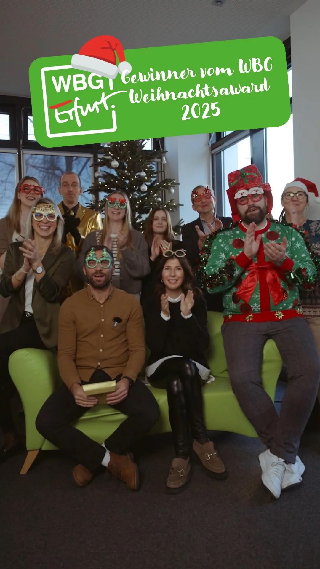Mitarbeitende der WBG Erfurt sitzen vor einem Weihnachtsbaum auf einem Sofa und applaudieren