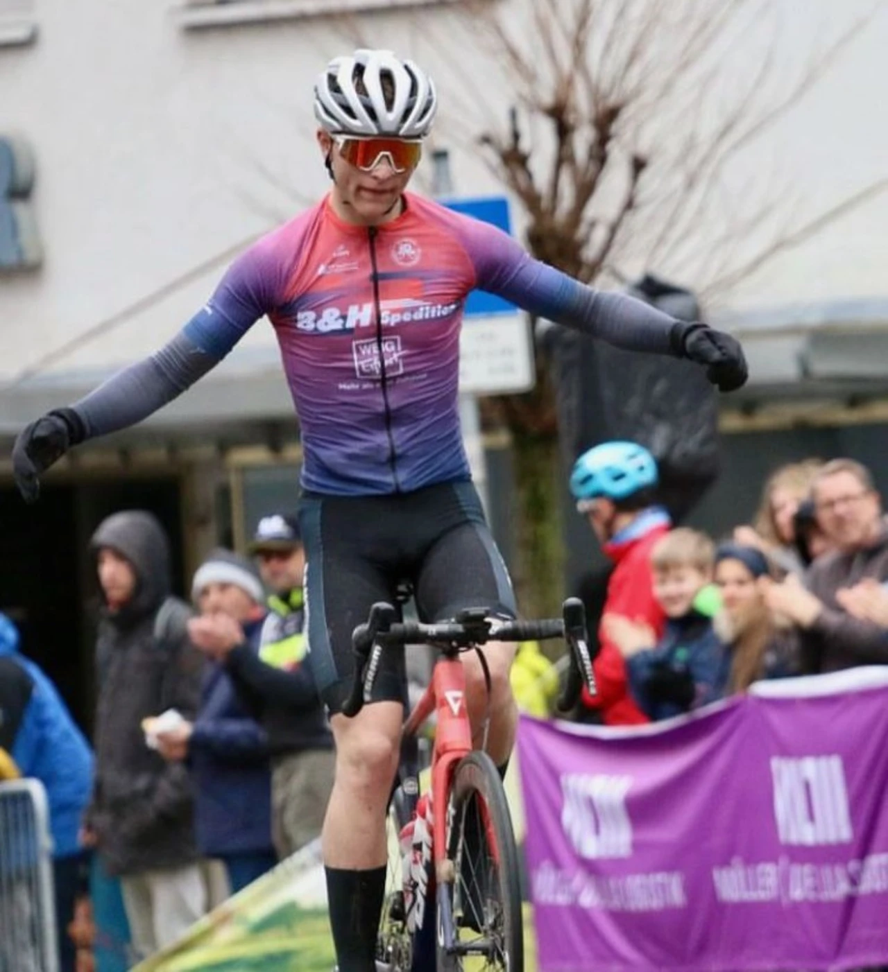 German Junior Racing Radrennfahrer jubelt beim Zieleinlauf vor applaudierendem Publikum
