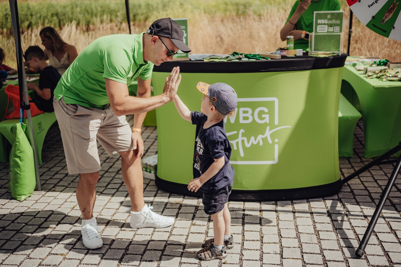Mitarbeiter der WBG Erfurt gibt einem kleinen Jungen beim Sommerfest einen High-Five, im Hintergrund stehen Messestand und Infomaterial