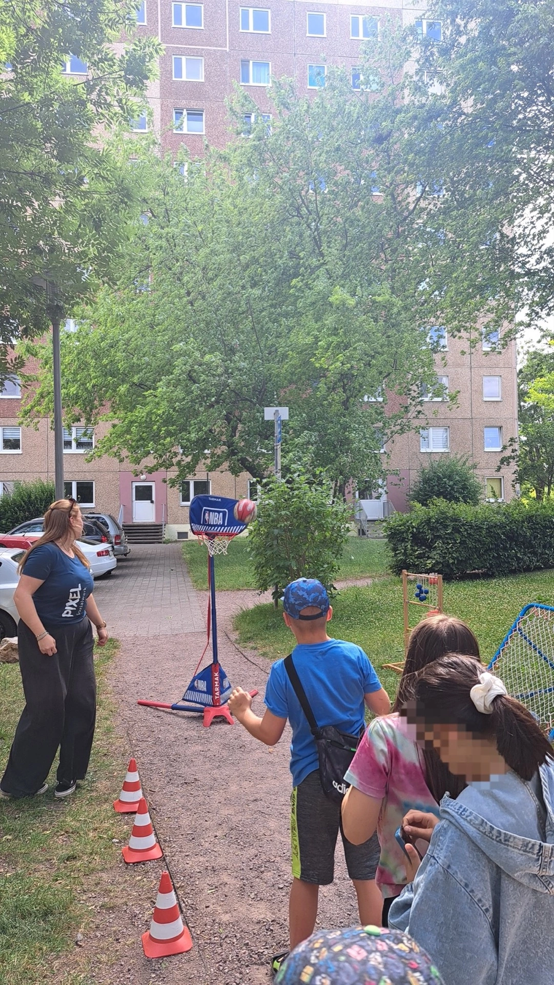 Kinder spielen Basketball auf einer Grünfläche vor einem Wohnblock
