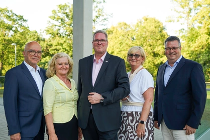 Fünf Personen in formeller Kleidung stehen für ein Gruppenfoto im Grünen