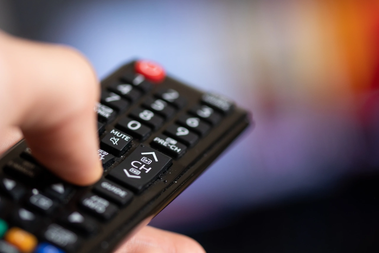 Nahaufnahme einer Hand, die eine TV-Fernbedienung bedient