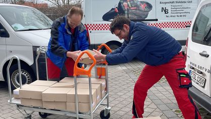 Zwei Mitarbeiter verladen Pakete auf einen Plattformwagen