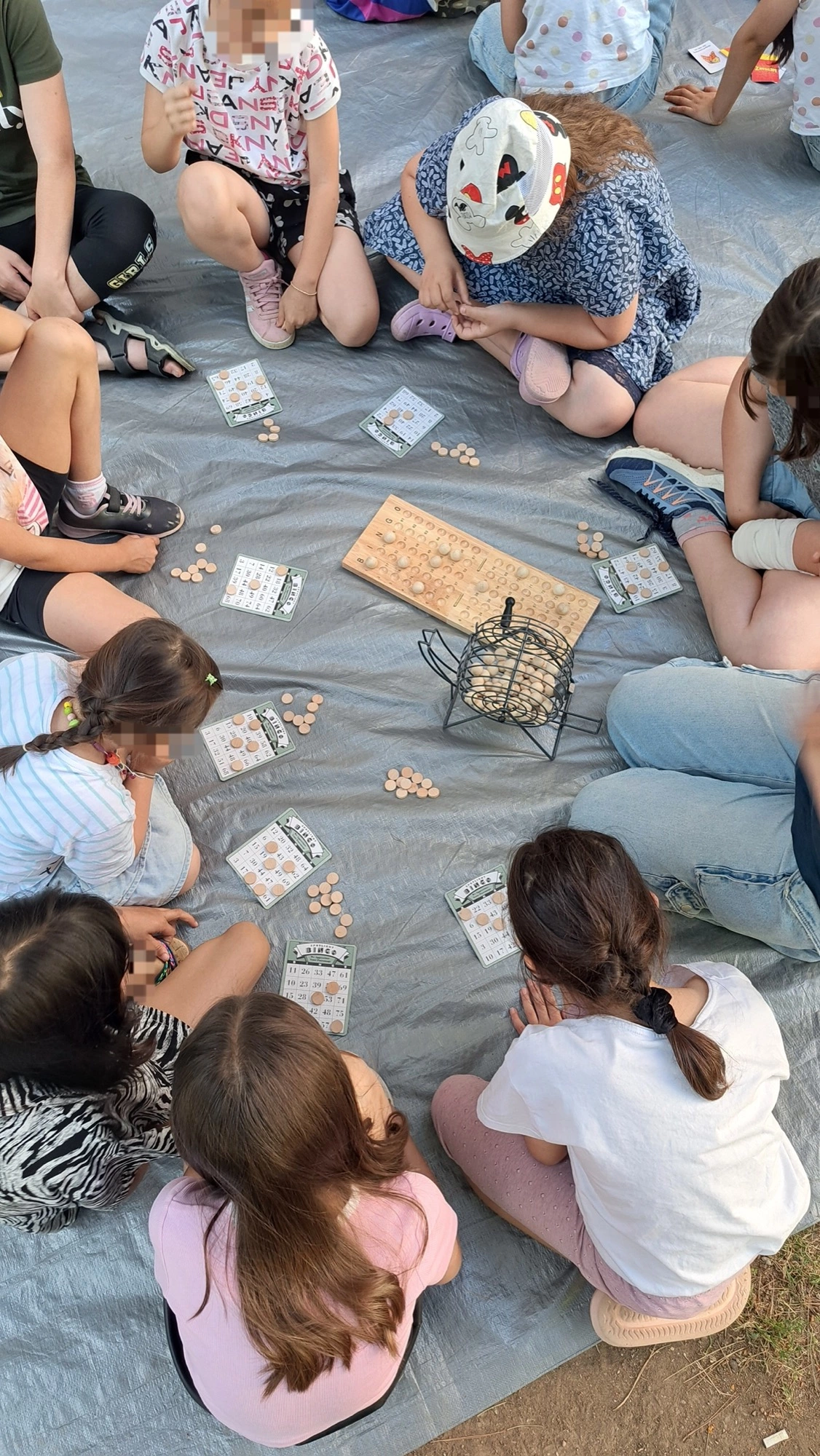 Kinder sitzen im Kreis auf einer Plane und spielen gemeinsam Bingo