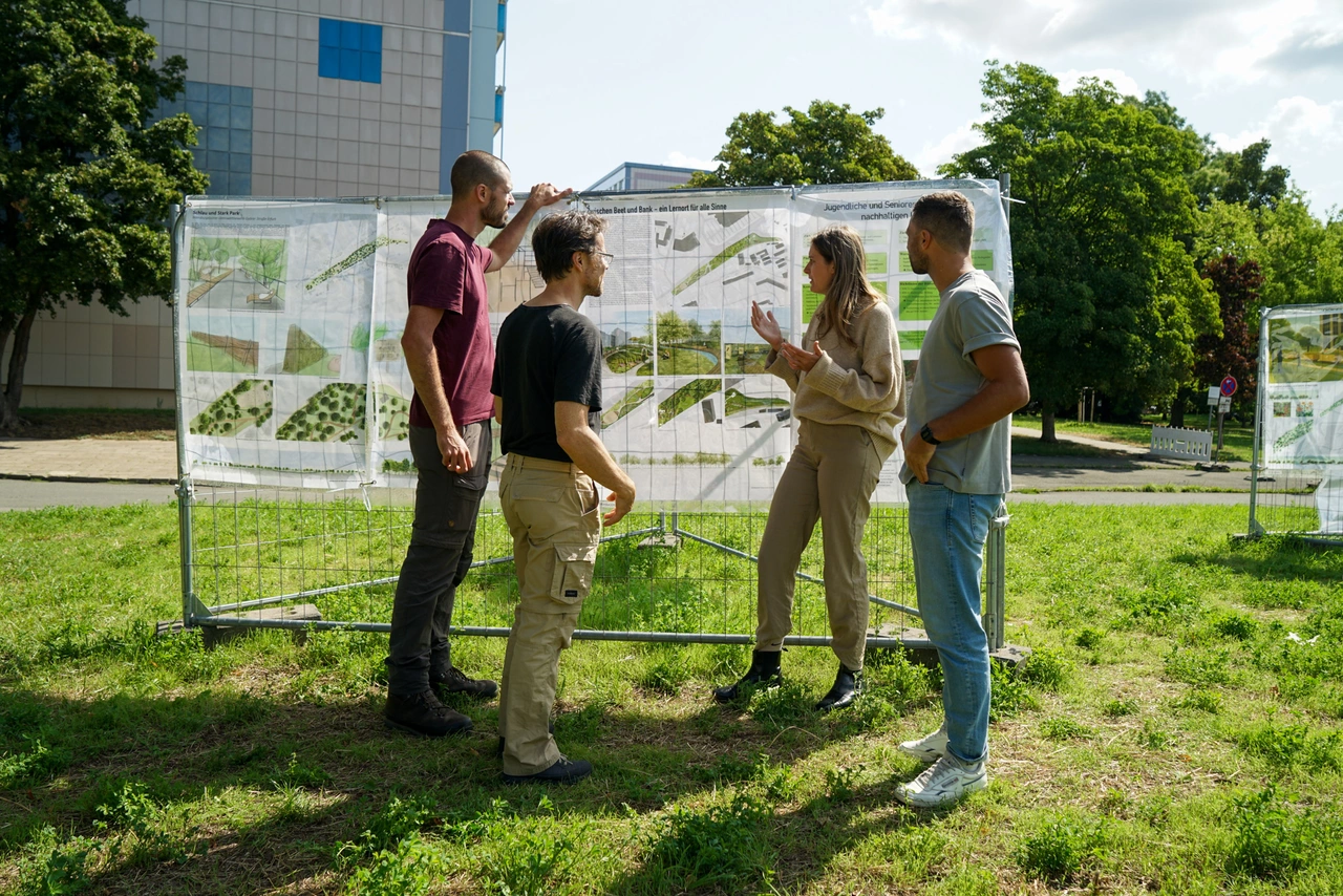Vier Personen stehen vor einer Infotafel und unterhalten sich