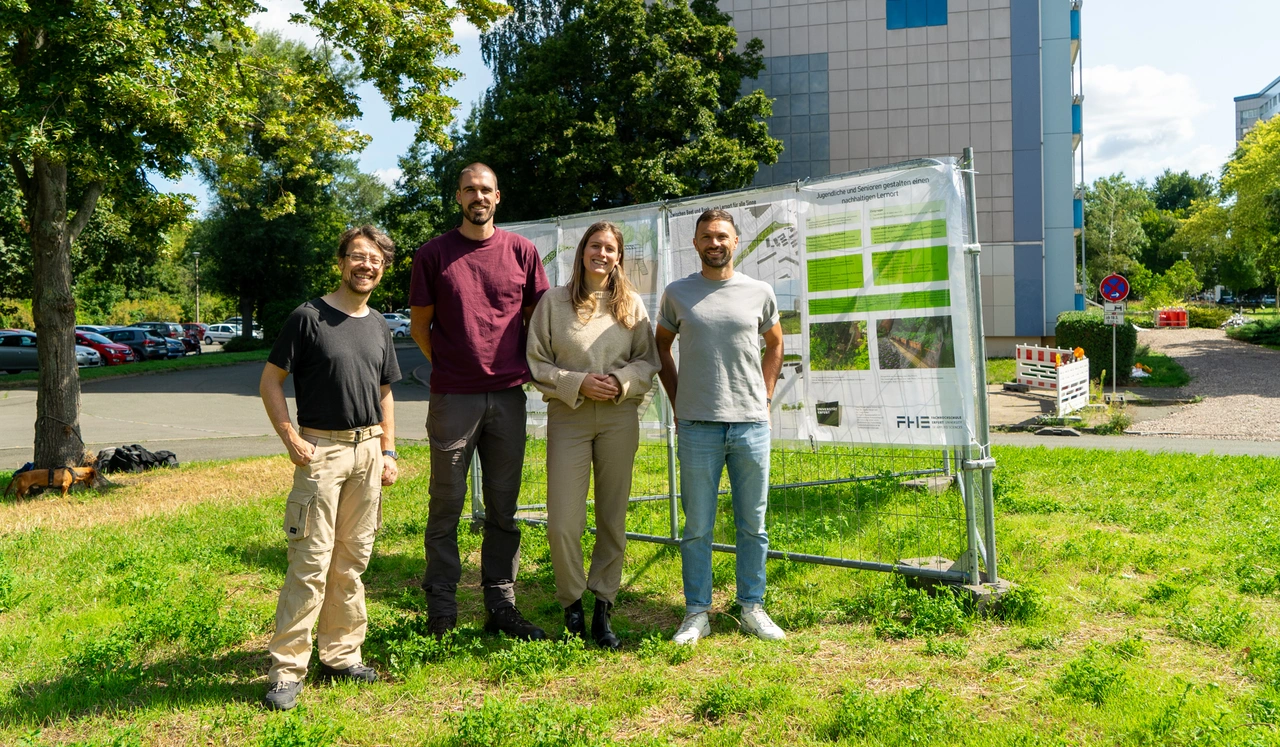 Projektteam Quartiersgestaltung Györer Straßw Vier Personen stehen lächelnd auf einer Wiese vor einer Infotafel zur Quartiersgestaltung in Erfurt