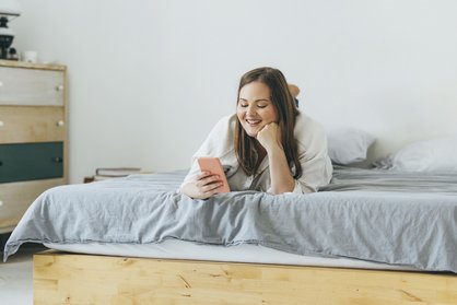 Junge Frau liegt auf einer Matratze und schaut aufs Handy