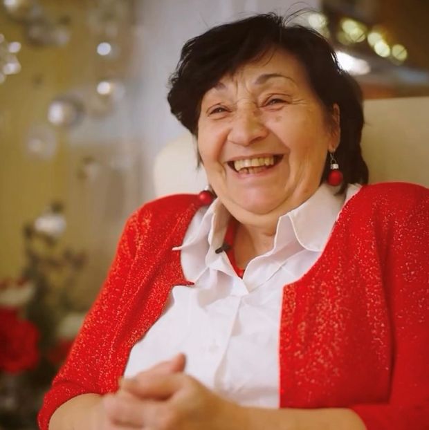 Ältere Frau mit weißer Bluse und einen glitzernden roten Cardigan sitzt vor Weihnachtsdekorationen in einem gemütlichen Raum